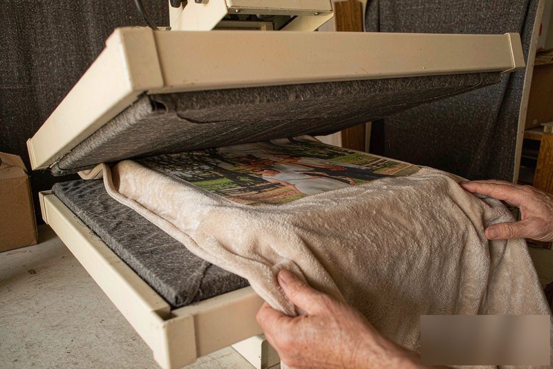 A custom photo design being printed onto fleece blanket fabric by a sublimation printer, with hands guiding the fabric